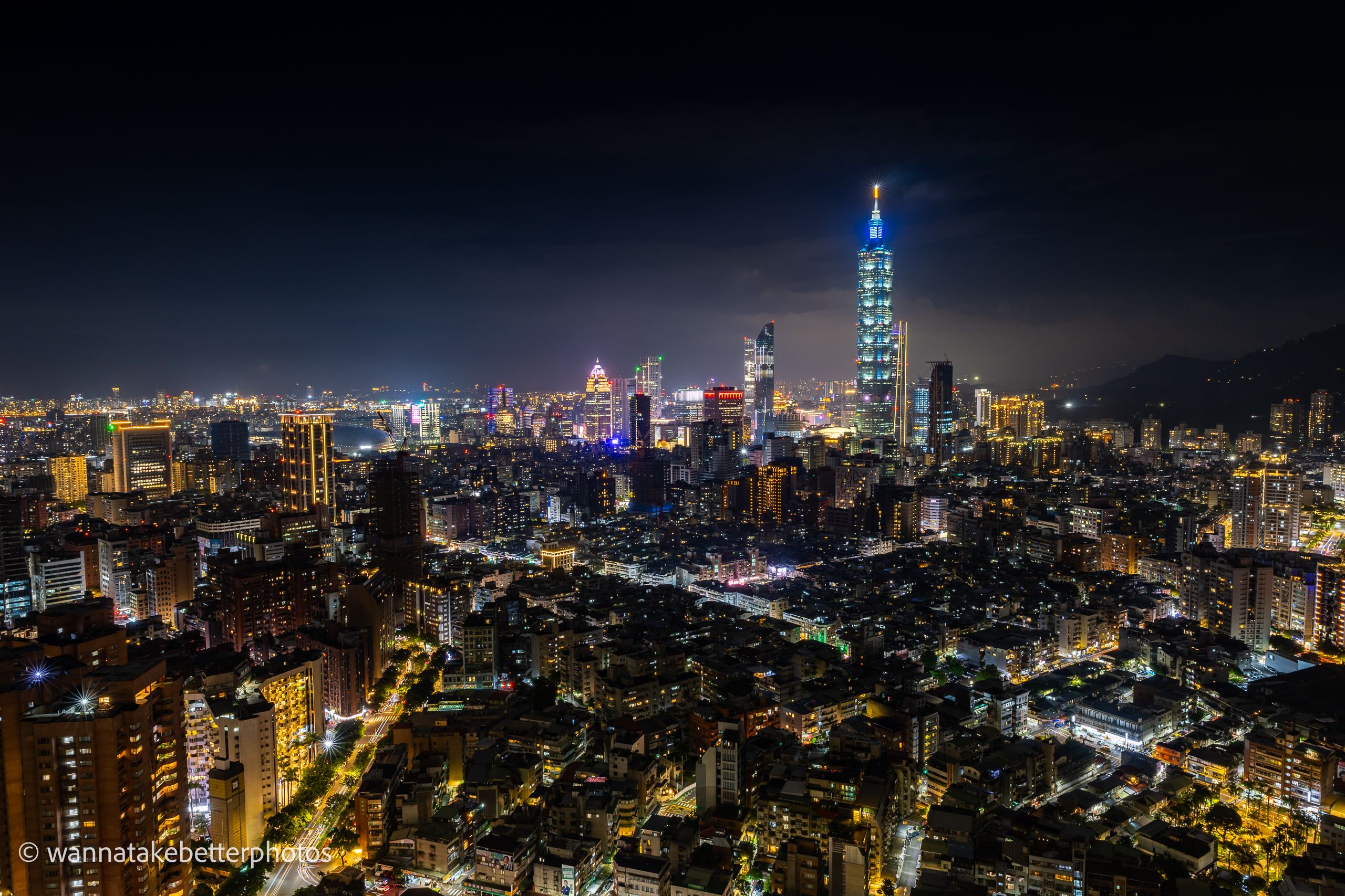A wide nighttime view of Taipei, with Taipei 101 glowing above the surrounding city